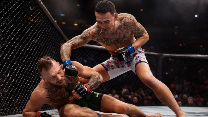 Max Holloway celebrates after defeating Conor McGregor by injury TKO at UFC 329, as McGregor reacts to his knee injury in the Octagon.